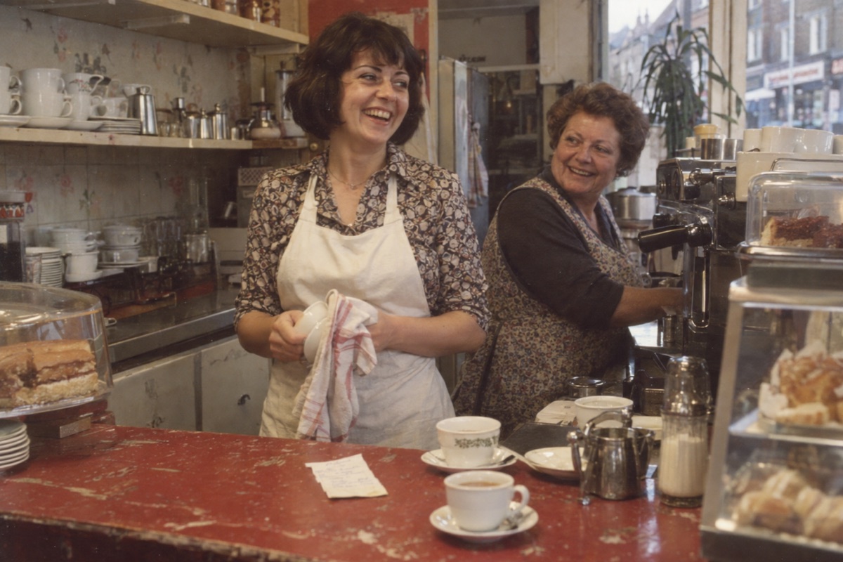 Fictional 1974 snapshot of Ilona and a coworker laughing behind a London cafe counter