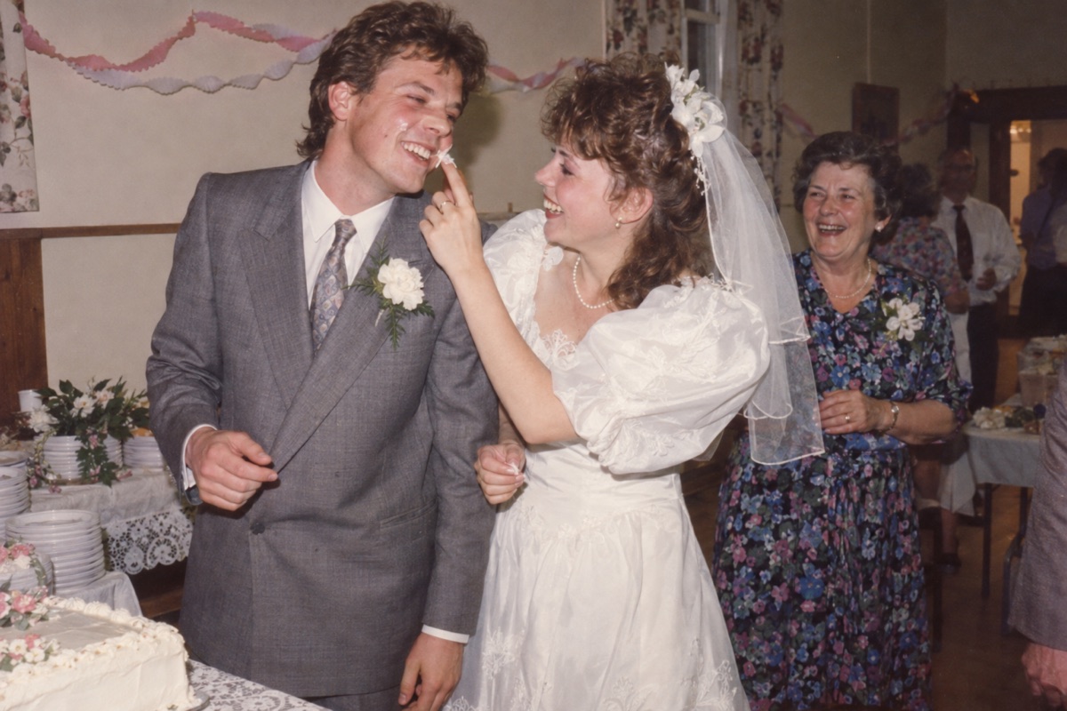 Fictional 1986 wedding snapshot of a couple laughing over cake